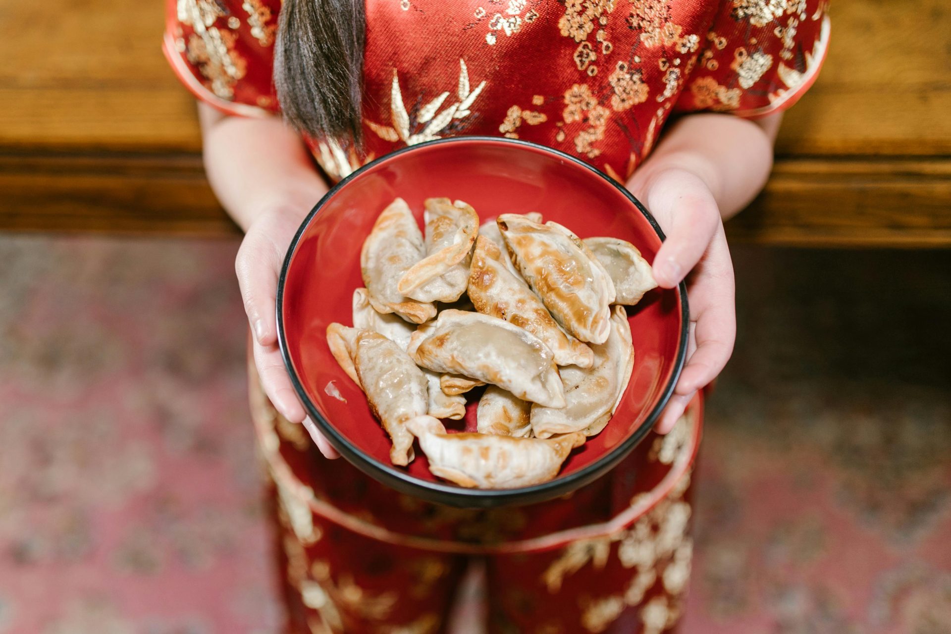 Person in red attire holding a bowl of Asian dumplings, food photography focus.